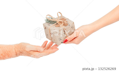Close-up of young female hands giving a small eco-friendly gift wrapped. pine twig to elderly hands concept of kindness, care intergenerational connection, isolated on white 132526269
