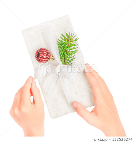 Hands holding white Christmas gift box decorated with a white ribbon, evergreen twig, red bauble ornament. Minimal festive composition isolated on white symbolizing holiday giving winter celebration Hands holding white Christmas gift box decorated with a white ribbon, evergreen twig, red bauble ornament. Minimal festive composition isolated on white symbolizing holiday giving winter celebration 132526274