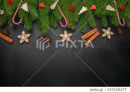 Christmas background with gingerbread cookies, cinnamon sticks, anise stars, fir branches and candy canes on black surface, festive flat lay with copy space for text Christmas background with gingerbread cookies, cinnamon sticks, anise stars, fir branches and candy canes on black surface, festive flat lay with copy space for text 132526277