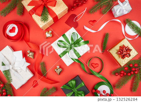 Festive Christmas flat lay colorful gift boxes wrapped in red, green, gold, and white ribbons on red background, decorated with fir branches, berries, and ornaments copy space 132526284