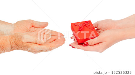 Young female hands offering a small red gift box with a bow to elderly hands waiting to receive it symbol of care, love, kindness, and intergenerational connection, isolated on white Young female hands offering a small red gift box with a bow to elderly hands waiting to receive it symbol of care, love, kindness, and intergenerational connection, isolated on white 132526323