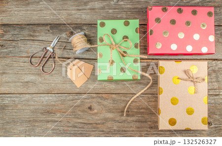 Colorful Christmas gift wrapping with golden polka dot boxes, twine, tags, and scissors on rustic wooden background with copy space 132526327