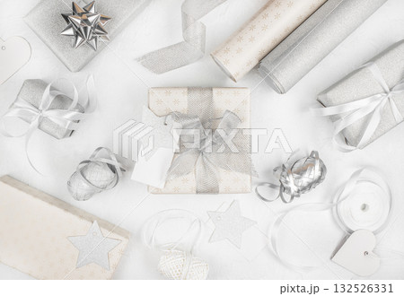 Stylish silver and white Christmas gift wrapping arrangement with ribbons, bows, and tags on light background, top view, festive flat lay 132526331