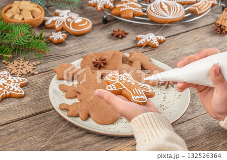 Christmas cookie decorating concept with hands piping icing on a festive gingerbread man on a rustic wooden background 132526364