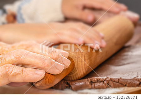 Close-up of elderly and young hands rolling gingerbread dough together, symbolizing generational connection, family tradition, and shared holiday moments Close-up of elderly and young hands rolling gingerbread dough together, symbolizing generational connection, family tradition, and shared holiday moments 132526371