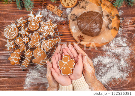 Generational family bonding and holiday baking concept with elderly and young hands holding a gingerbread angel cookie together, symbolizing love, care, tradition, and Christmas spirit 132526381
