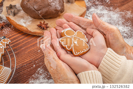 Generations united by love and tradition elderly and young hands gently holding a gingerbread angel cookie, symbolizing family, warmth, and the spirit of Christmas 132526382