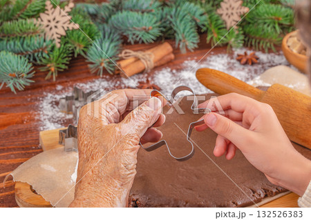 Generations connecting through holiday traditions elderly and young hands holding a gingerbread man cookie cutter over rolled dough, symbolizing family, love, and Christmas baking together. 132526383