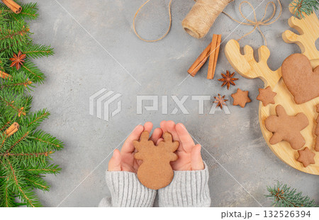 Cozy holiday concept with hands holding a reindeer-shaped gingerbread cookie surrounded by Christmas spices, fir branches, and copy space for festive greeting or seasonal design Cozy holiday concept with hands holding a reindeer-shaped gingerbread cookie surrounded by Christmas spices, fir branches, and copy space for festive greeting or seasonal design 132526394