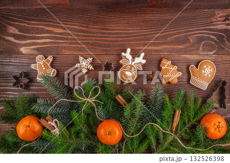 Festive Christmas composition with gingerbread cookies, fir branches, tangerines, and spices on a wooden background, perfect for holiday design and seasonal advertising 132526398