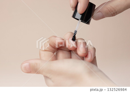 Manicure with colorless protective varnish. Woman paints her nails. Nude background copy space photo close up Manicure with colorless protective varnish. Woman paints her nails. Nude background copy space photo close up 132526984