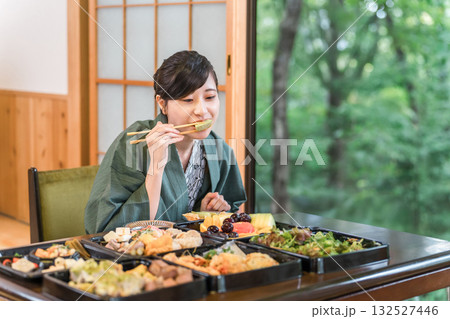 テーブルいっぱいの食事を嬉しそうに食べる浴衣姿の若い女性 132527446