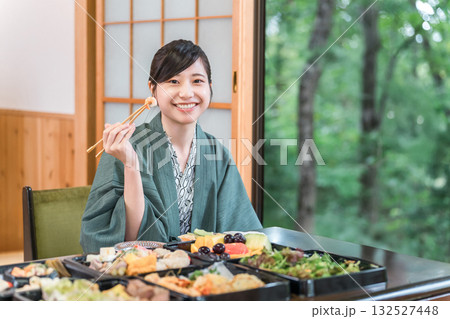 テーブルいっぱいの食事を嬉しそうに食べる浴衣姿の若い女性 132527448