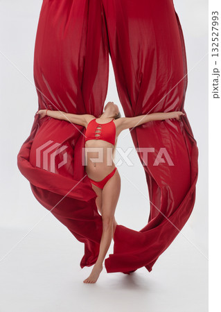 Model poses dramatically between large red drapes in a studio setting 132527993