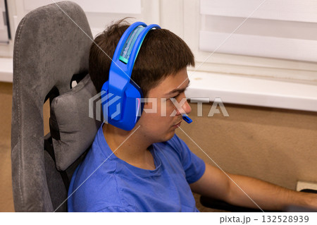 Digital meditation concept - gamer achieves flow state during intense gameplay. Blue headphones create sonic isolation, focused mind in comfortable gaming chair represents modern concentration 132528939
