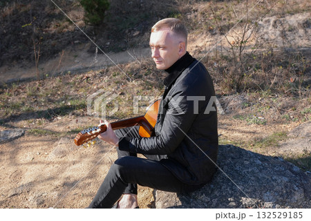 Blonde man playing string guitar outdoors in autumn forest. Concept of sound therapy, mental health and wellness rituals. Calmness tranquility audio-sensory practices. Aura farming energy Blonde man playing string guitar outdoors in autumn forest. Concept of sound therapy, mental health and wellness rituals. Calmness tranquility audio-sensory practices. Aura farming energy 132529185