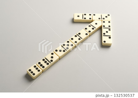 Domino pieces arranged in arrow shape symbolize business growth and success in strategic and creative way on plain background Domino pieces arranged in arrow shape symbolize business growth and success in strategic and creative way on plain background 132530537