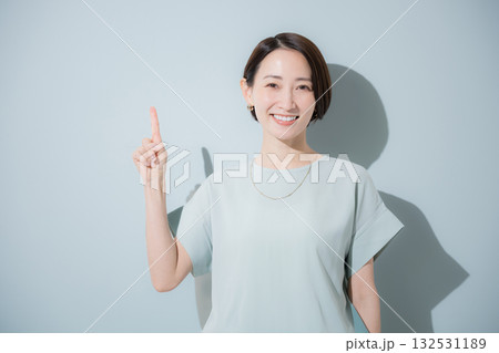 綺麗なミントグリーン背景のビジネス女性イメージ　上半身正面で指差しポイントポーズ 132531189
