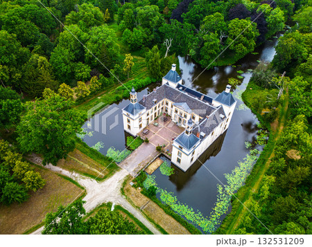 Aerial view of historic manor symmetrical design with chimneys set in forested landscape and open fields, autumn hues and warm sky tones create a serene, picturesque countryside scene. Aerial view of historic manor symmetrical design with chimneys set in forested landscape and open fields, autumn hues and warm sky tones create a serene, picturesque countryside scene. 132531209