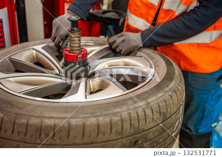 Car wheel positioned on a tire changing machine before removing the tire from the rim. Seasonal tire replacement process at an auto service during winter preparation. 132531771