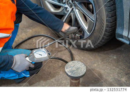 Worker checking tire pressure with gauge after seasonal wheel replacement. Final step of winter tire preparation in auto service in Czech Republic. 132531774