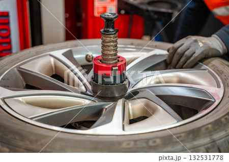 Car wheel positioned on a tire changing machine before removing the tire from the rim. Seasonal tire replacement process at an auto service during winter preparation. Car wheel positioned on a tire changing machine before removing the tire from the rim. Seasonal tire replacement process at an auto service during winter preparation. 132531778
