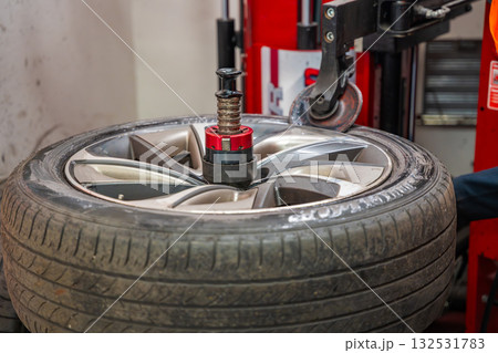 Tire changing machine removing the rubber tire from the rim using a rotating metal arm. Essential step in seasonal wheel replacement at a professional auto workshop. Tire changing machine removing the rubber tire from the rim using a rotating metal arm. Essential step in seasonal wheel replacement at a professional auto workshop. 132531783