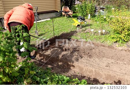 A retired farmer rakes the soil on a sunny autumn day 132532103