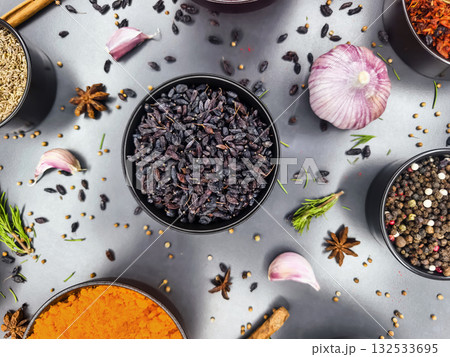 Collection of spices and herbs arranged in bowls with garlic and onion on a gray surface 132533695