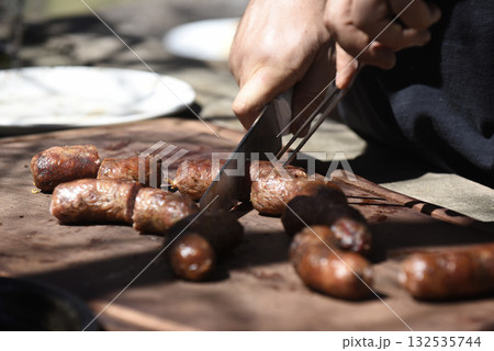 Hands cutting barbecue, grilled sausages and cow meat , traditional argentine cuisine 132535744
