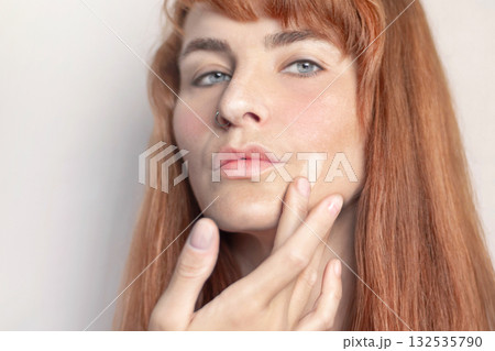 Red-haired caucasian girl puts foundation on her face with her finger white background Red-haired caucasian girl puts foundation on her face with her finger white background 132535790