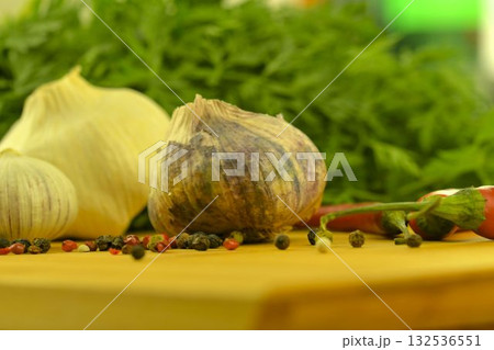 The bulbs of garlic, red chili peppers, four-color pepper, and carrot tops on a wooden cutting board. The concept of culinary arts and vegetables in the home. Macro image, close-up. Garlic - species 132536551