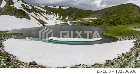The snow melts. Mountain peaks, green grass and cold lake 132536936