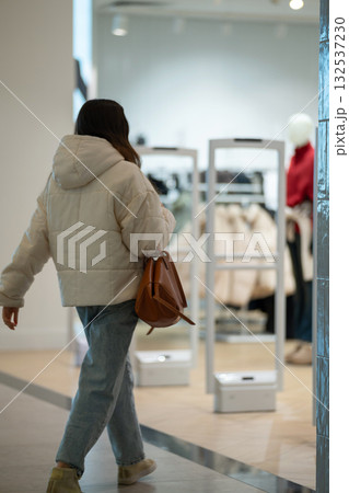 A woman with a brown handbag walks through a modern store entrance A woman with a brown handbag walks through a modern store entrance 132537230