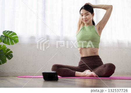 スマートフォンを見ながらストレッチをするミドル女性 スマートフォンを見ながらストレッチをするミドル女性 132537726