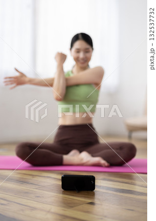 自宅でヨガのオンラインレッスンを受ける女性の前に置かれたスマートフォン 132537732