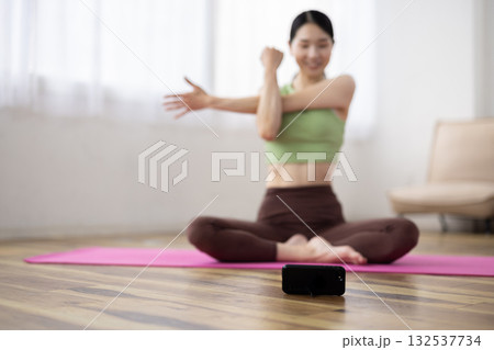 自宅でヨガのオンラインレッスンを受ける女性の前に置かれたスマートフォン 132537734