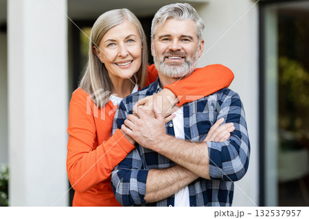 Cute woman in orange shirt hugging her husband and smiling nicely Cute woman in orange shirt hugging her husband and smiling nicely 132537957