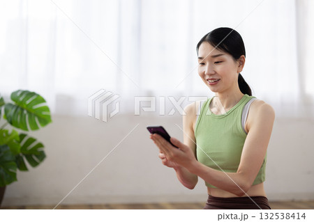 スマートフォンを操作し微笑むヨガウェアを着たミドル女性 132538414