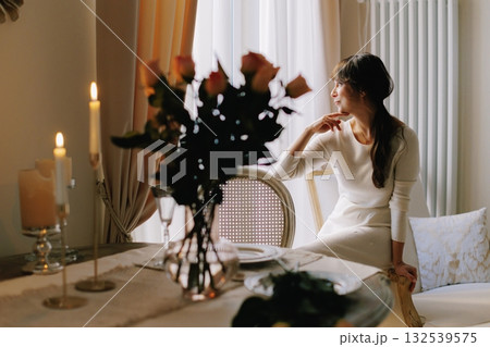 Woman sitting at a table with lit candles and flowers, contemplating during an elegant dinner setting Woman sitting at a table with lit candles and flowers, contemplating during an elegant dinner setting 132539575