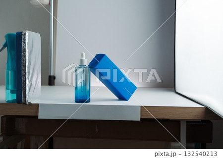 Behind-the-scenes view of product photography setup with softbox, white background, and reflector propped on a spray bottle, mobile photo. Concept of studio, lighting, photography, setup. 132540213