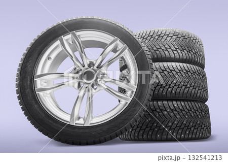 Four studded winter tires stacked beside an alloy rim display the necessary equipment for winter driving. This setup is ideal for tire replacement in colder conditions. Four studded winter tires stacked beside an alloy rim display the necessary equipment for winter driving. This setup is ideal for tire replacement in colder conditions. 132541213