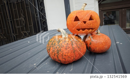 Three pumpkins arranged outdoors with one carved into a jack-o'-lantern featuring a smiling face. The image represents Halloween decoration, autumn celebration, and seasonal creativity 132541569