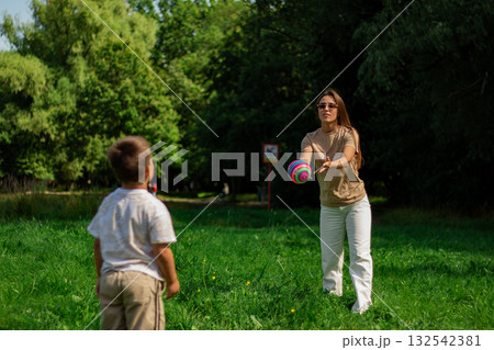Active lifestyle of mom and son. Energetic scene of mother and boy running and kicking ball on sunny day. Ideal for themes of health, fitness, sports, and active living for all ages. 132542381