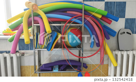 Colorful pool noodles, kickboards, hoops, and a beach ball organized on metal shelves in a swimming pool area, ready for fun water activities and summer training.  132542418