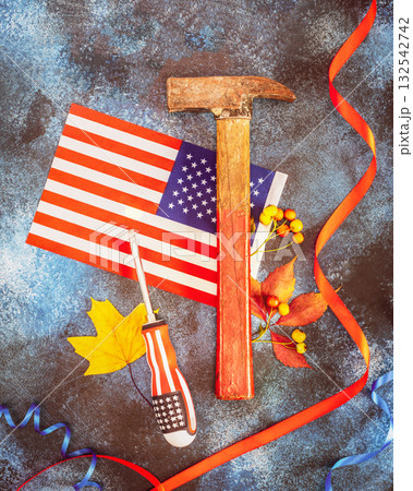 Labor Day card with american flag, hammer, screwdriver, autumn leaves and red ribbon on a blue textured background. Labor day is America and Canada traditional holiday. Flat lay Labor Day card with american flag, hammer, screwdriver, autumn leaves and red ribbon on a blue textured background. Labor day is America and Canada traditional holiday. Flat lay 132542742