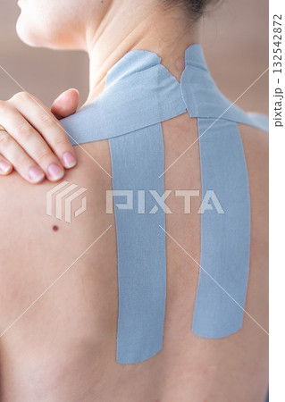 Close-up of kinesiology tape applied to the shoulder and neck, with a woman hand resting on the taped area. Pain relief and self-care through therapeutic taping techniques. 132542872