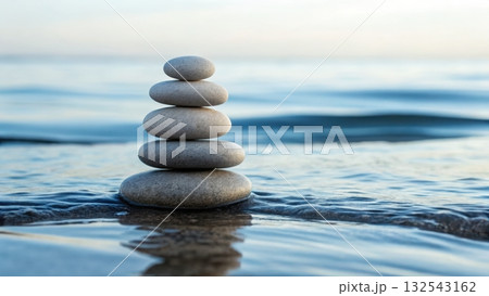 Smooth balanced stones carefully stacked on peaceful shoreline with gentle waves in the background Smooth balanced stones carefully stacked on peaceful shoreline with gentle waves in the background 132543162