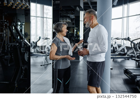 Mature man and woman are having a conversation while resting in a gym Mature man and woman are having a conversation while resting in a gym 132544750