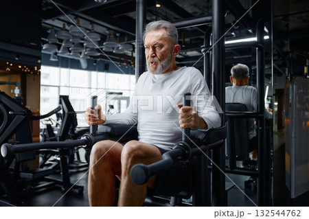 An older gentleman is actively exercising on a machine at a gym An older gentleman is actively exercising on a machine at a gym 132544762